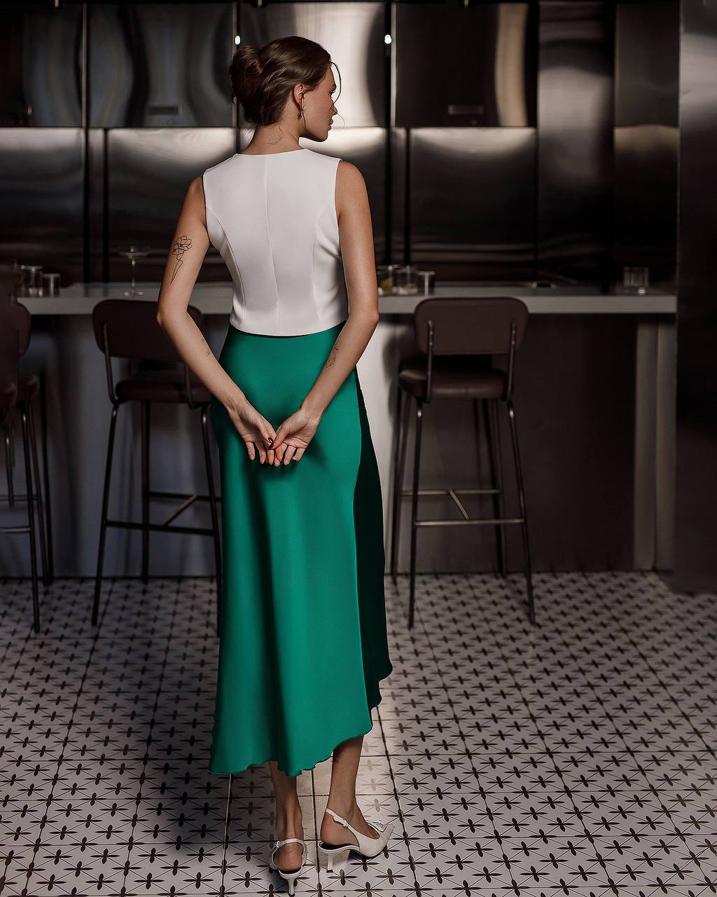 Woman in a white top and teal skirt standing in a modern kitchen.
