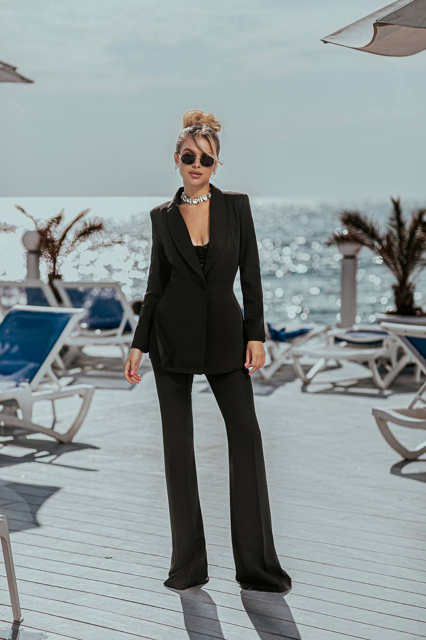 Woman in a black suit standing on a deck with ocean view