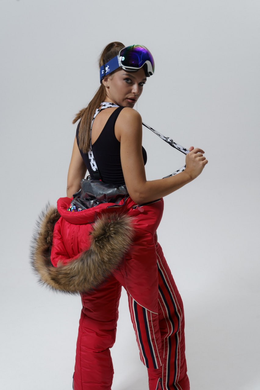 Person wearing a black top, red pants with fur trim, and goggles on a plain background