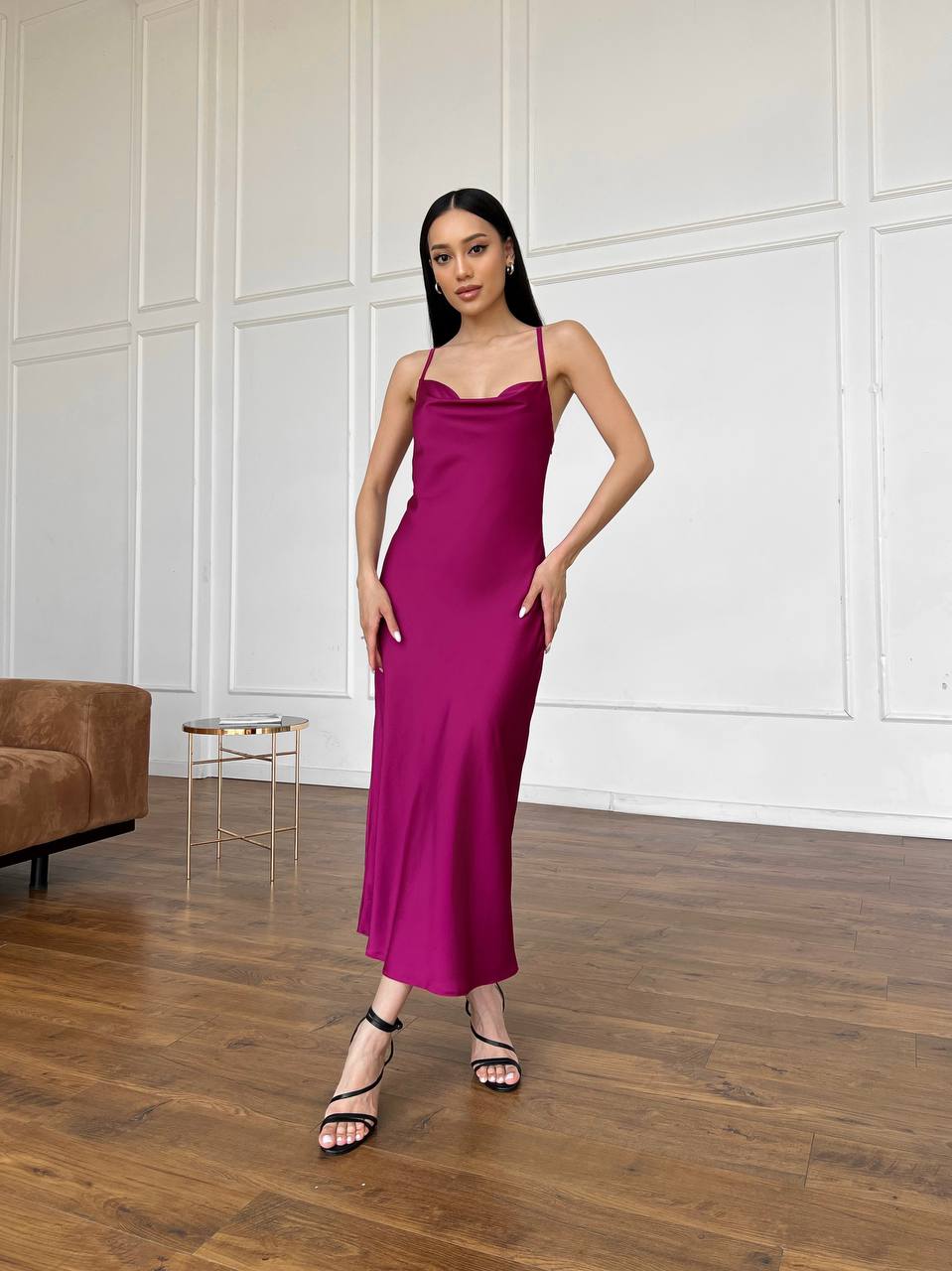 Woman in a magenta dress standing in a room with wooden flooring and a white paneled wall.