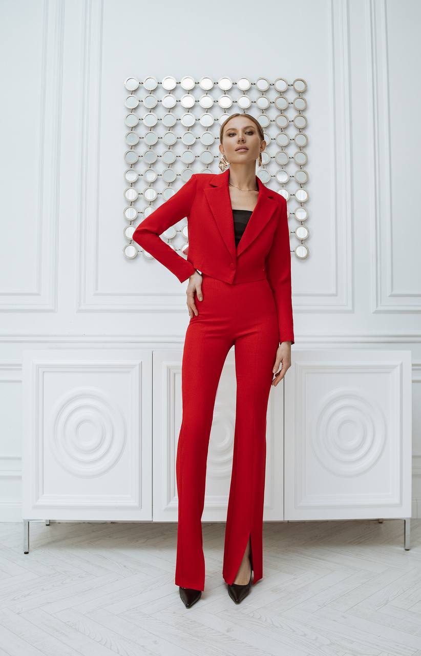 Woman wearing a red suit standing against a white wall with decorative patterns.