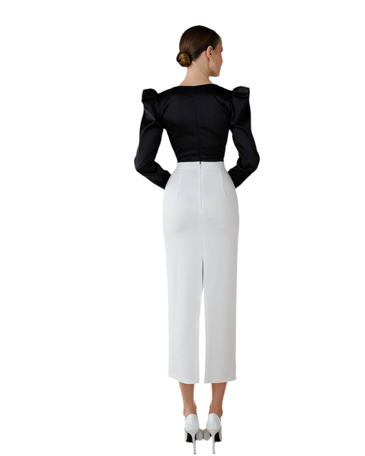 Woman wearing a black top with puffed sleeves and white pants on a white background