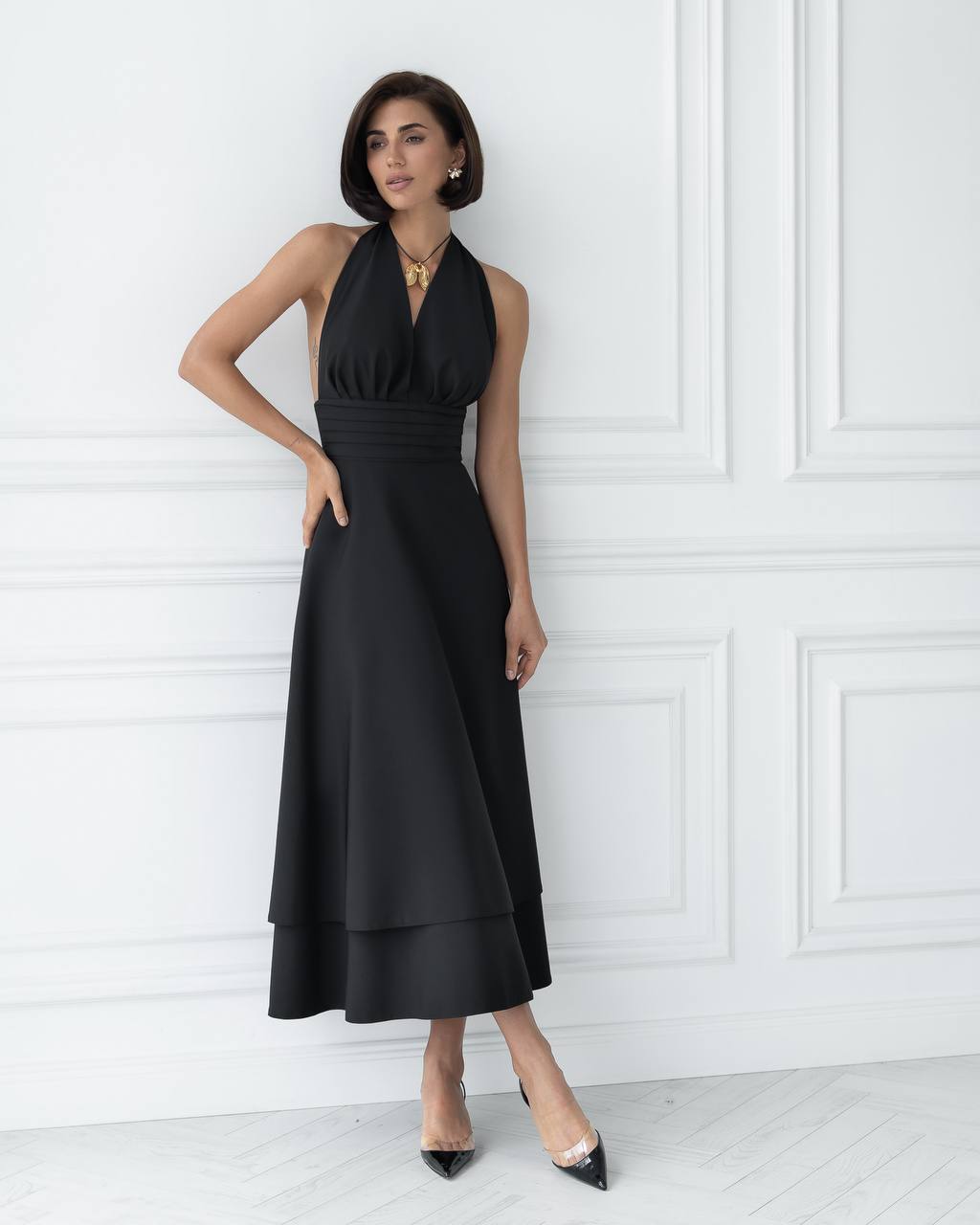 Woman wearing a black halter neck dress against a white wall.