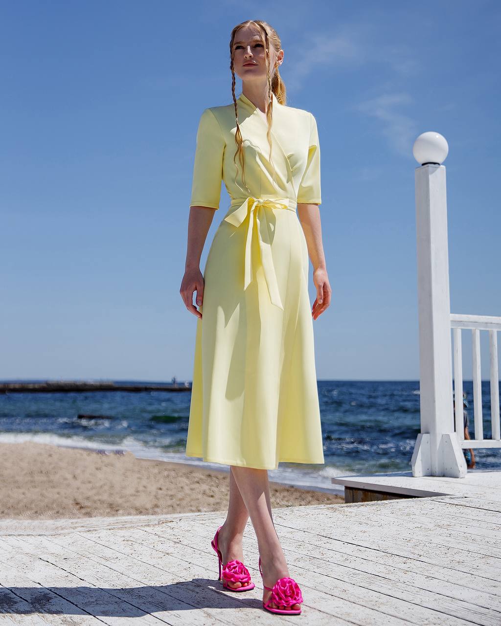 Woman in a yellow dress standing on a wooden deck by the ocean.