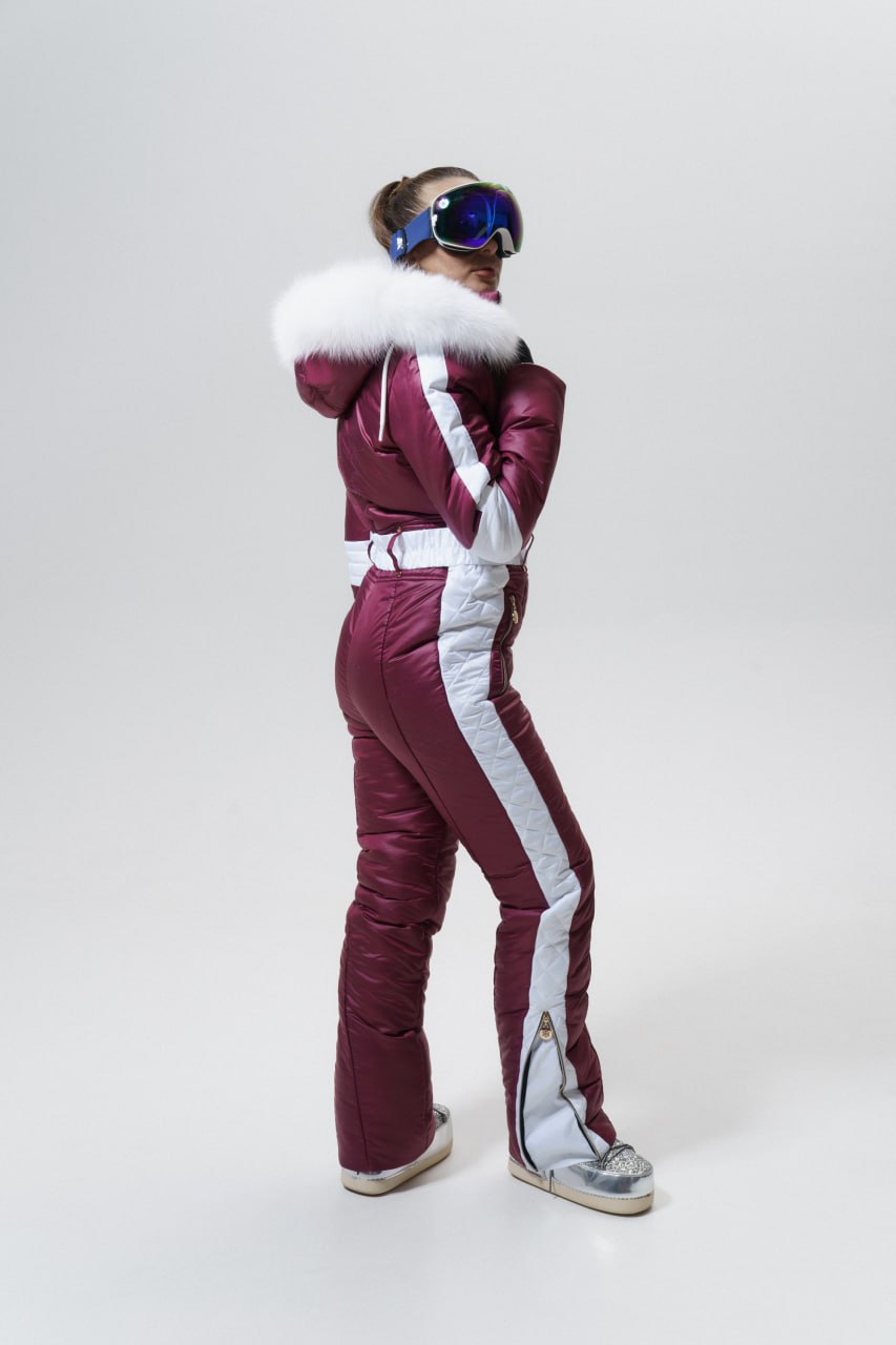 Person wearing a maroon and white ski suit with goggles on a white background