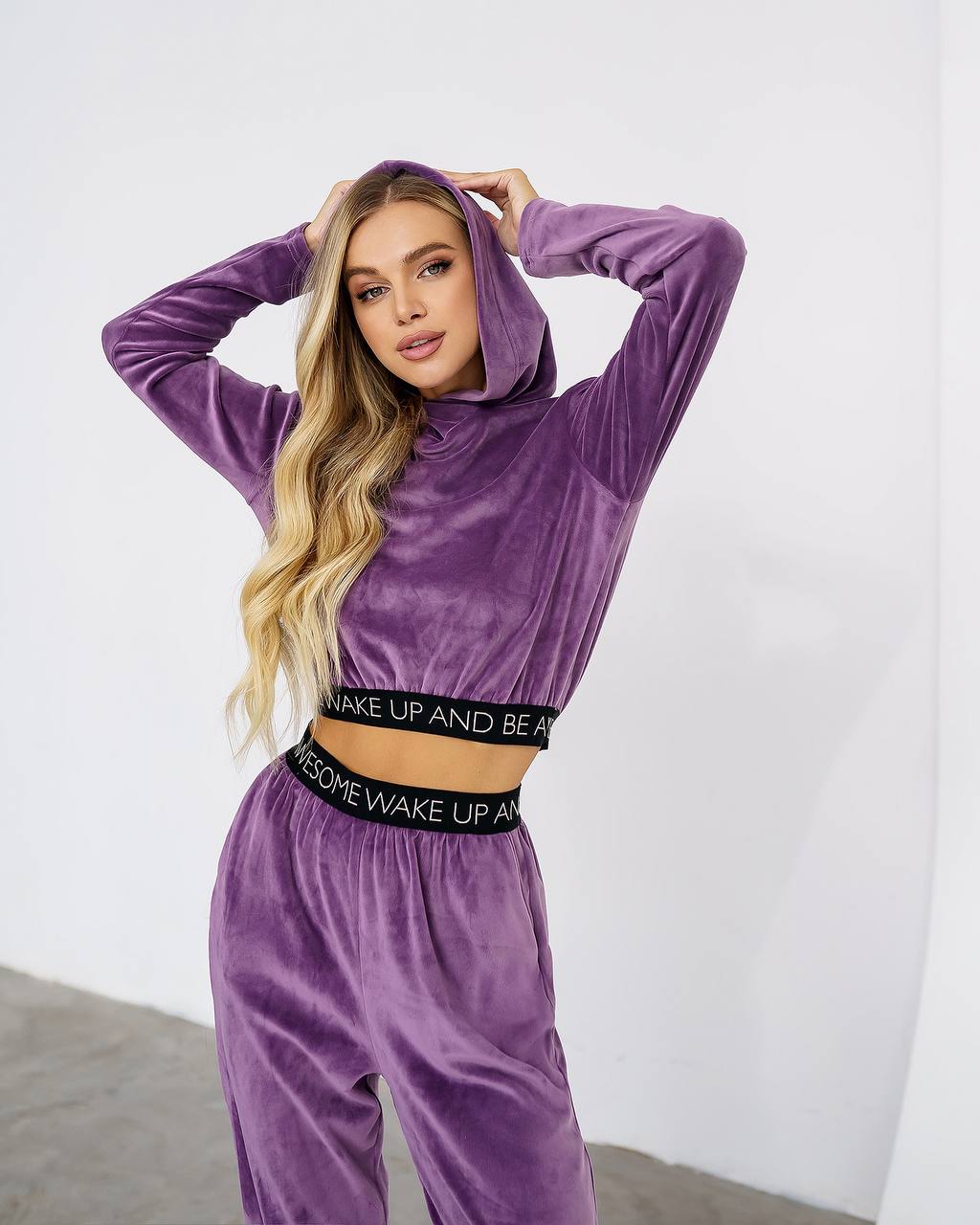 Woman wearing a purple velour tracksuit with text on the waistband against a white background