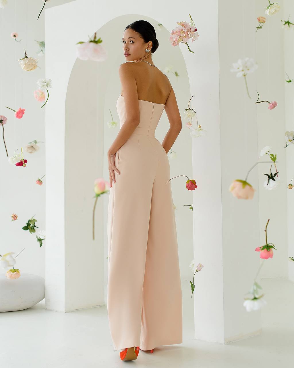 Woman in a strapless beige gown standing in a room with floral decorations.