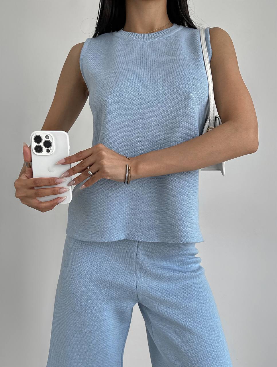 Person wearing a light blue sleeveless top and pants, holding a phone with a gray background