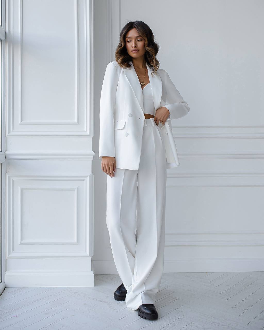 Woman wearing a white suit standing in a minimalistic room with white walls and floor.