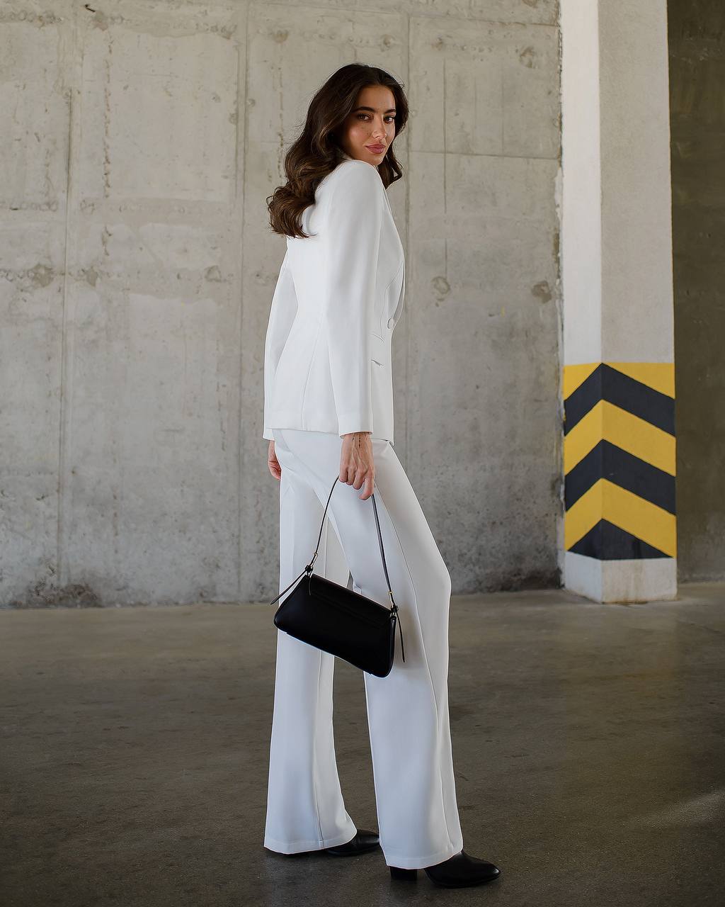 Woman in a white outfit with a black handbag standing in an industrial setting.