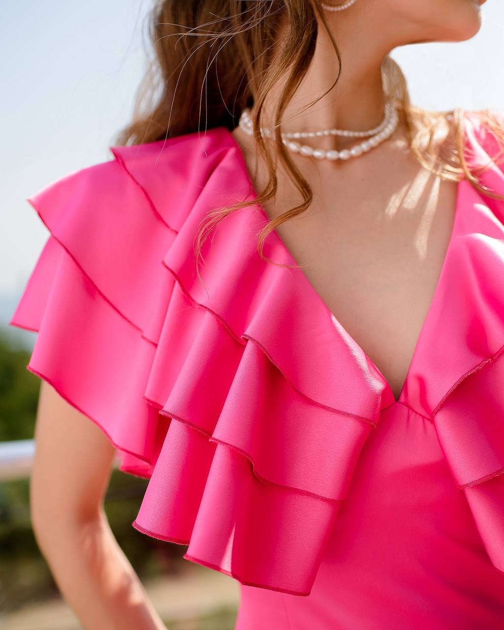 Close-up of a person wearing a bright pink ruffled top with a blurred natural background