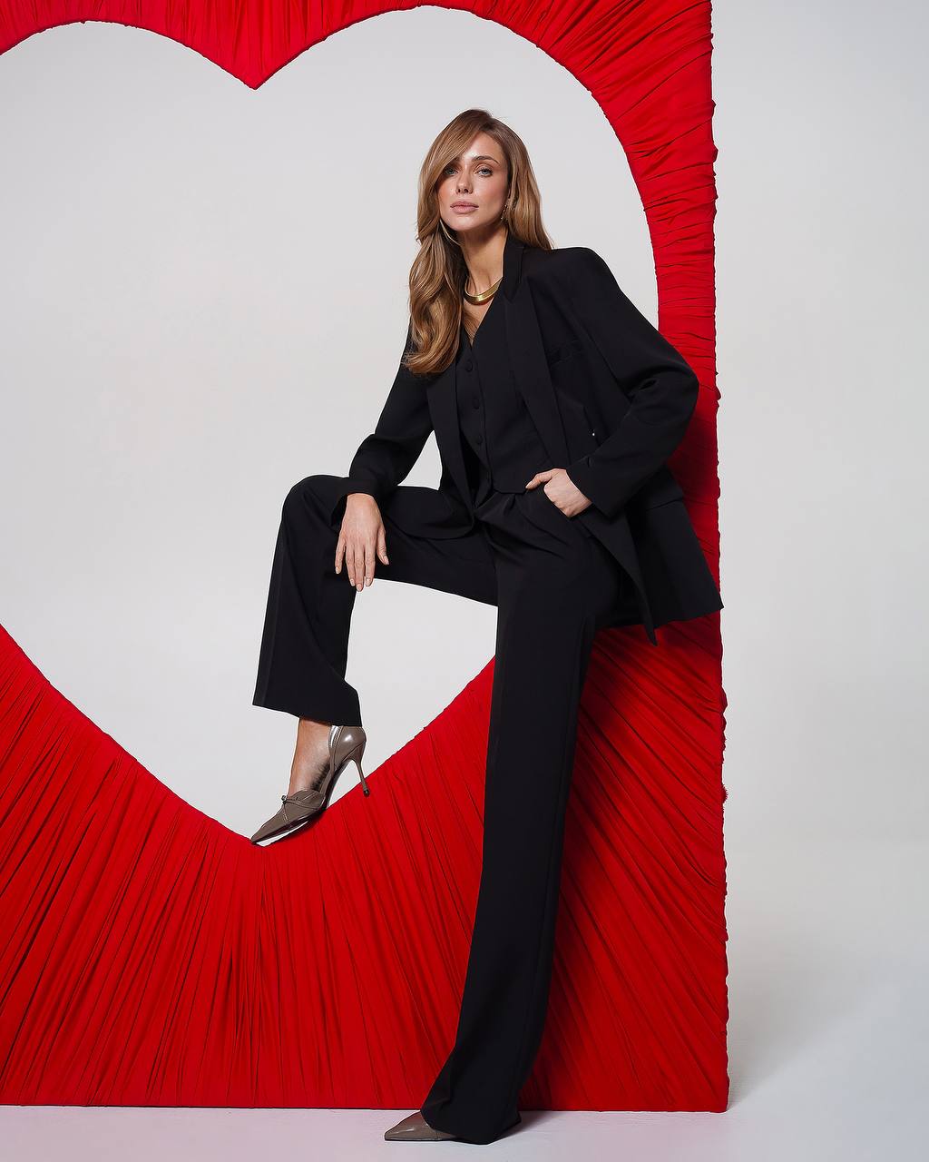 Woman in a black outfit sitting against a red heart-shaped backdrop