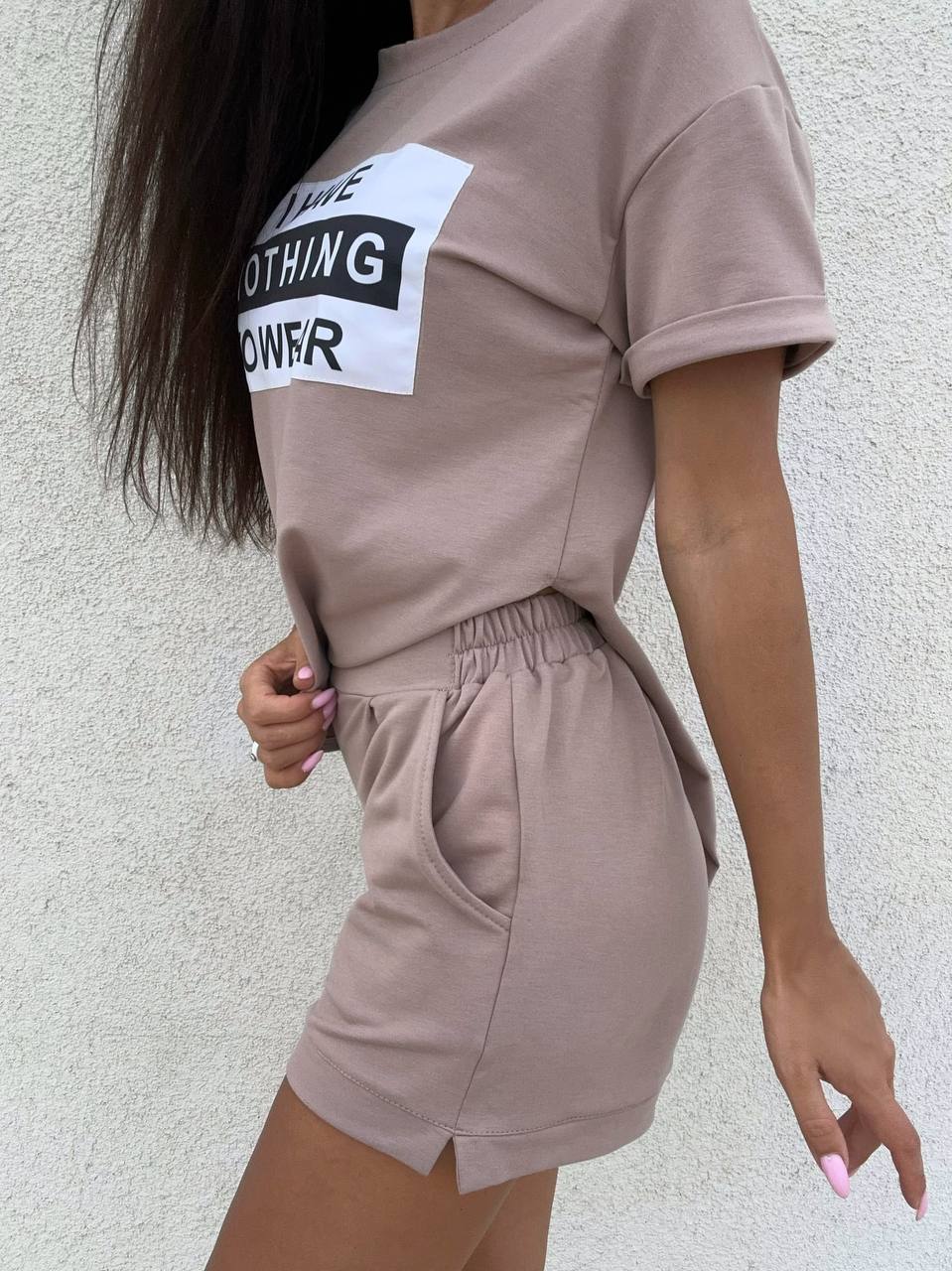 Person wearing a beige outfit with a graphic tee and shorts against a light background
