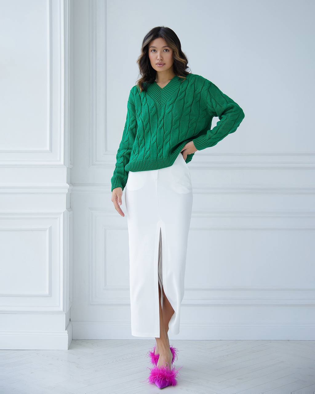 Woman wearing a green sweater and white skirt with pink shoes against a white background