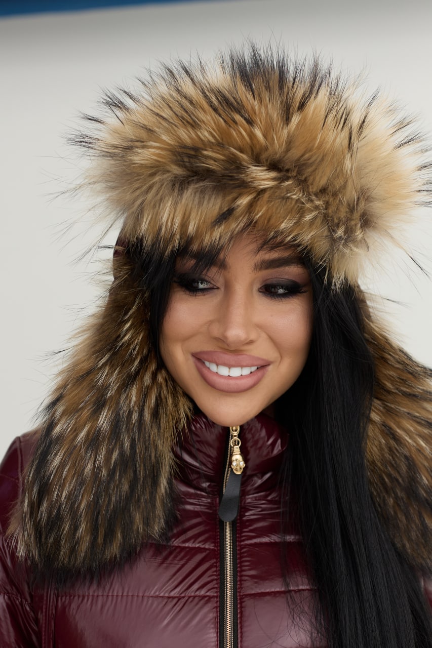 Person wearing a maroon puffer jacket with a fur-lined hood against a neutral background