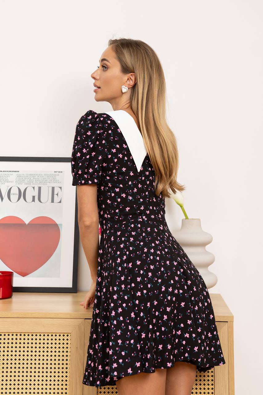 Woman wearing a black floral dress with a white collar in a room with a Vogue magazine and heart graphic.