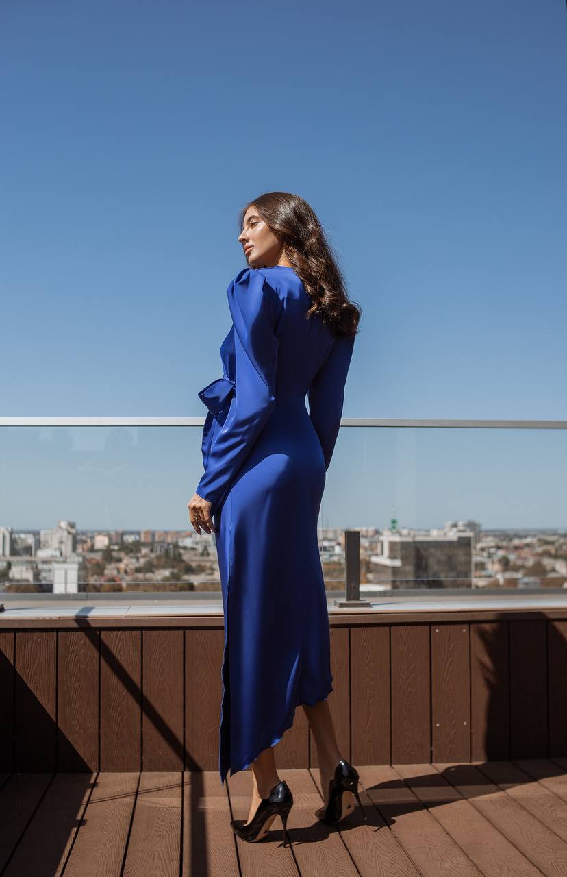 Woman in a blue dress standing on a rooftop with a cityscape in the background