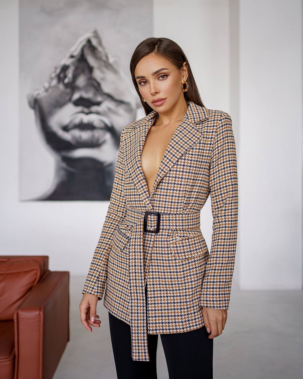 Woman wearing a checkered blazer with a belt in an indoor setting.