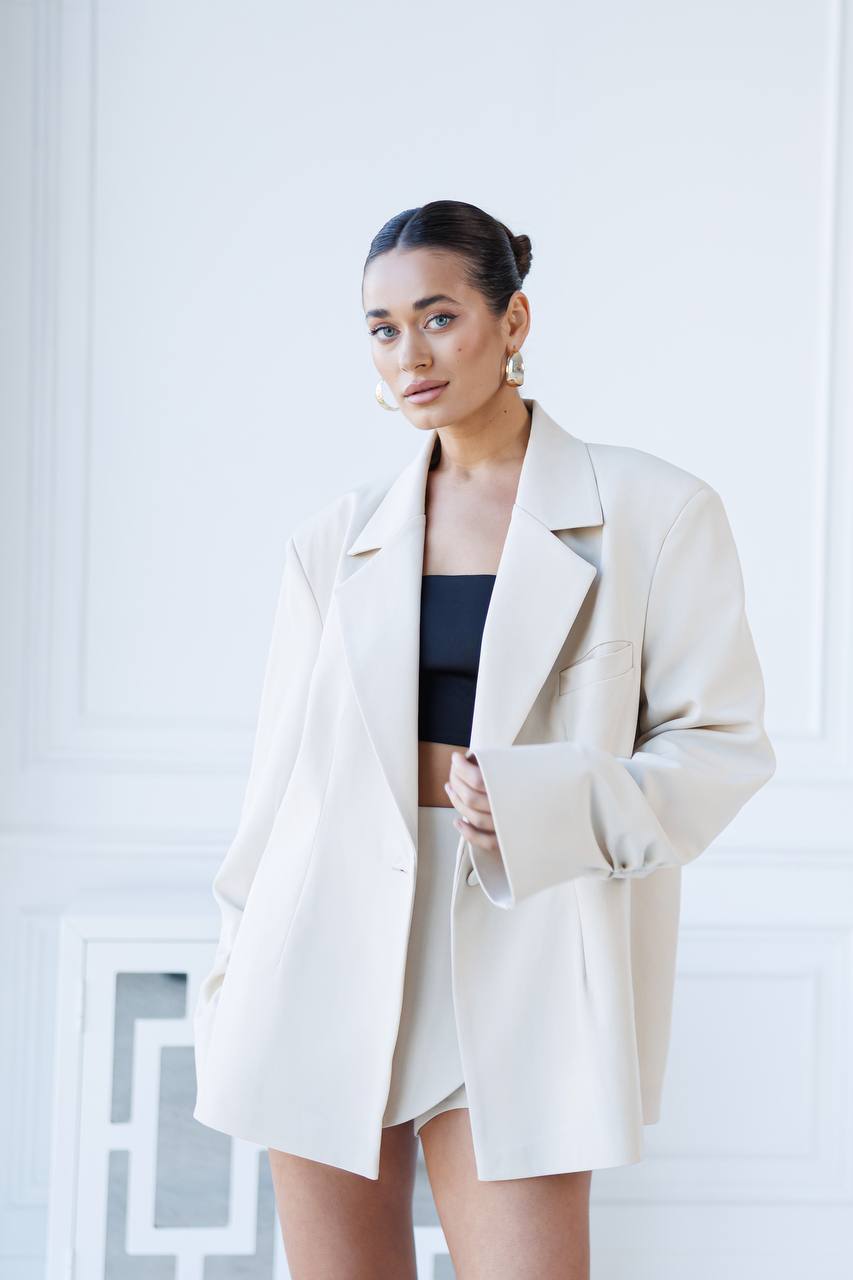 Woman wearing a beige coat over a black top and skirt in a minimalistic setting