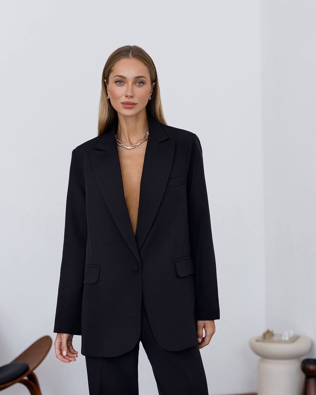 Person wearing a black blazer over a sheer top against a plain background