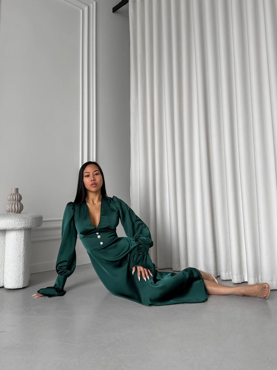 Woman in a green dress sitting on the floor against a white curtain.