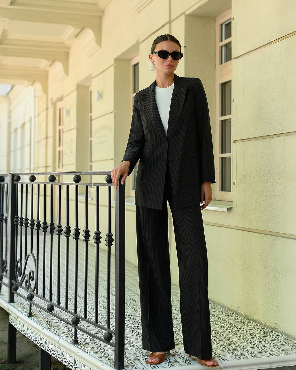Person wearing a black suit standing on a balcony with classical architecture in the background