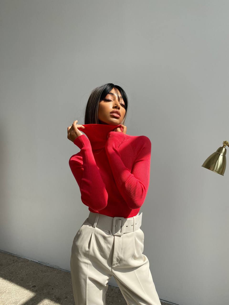 Person wearing a red sweater and beige pants against a plain wall.