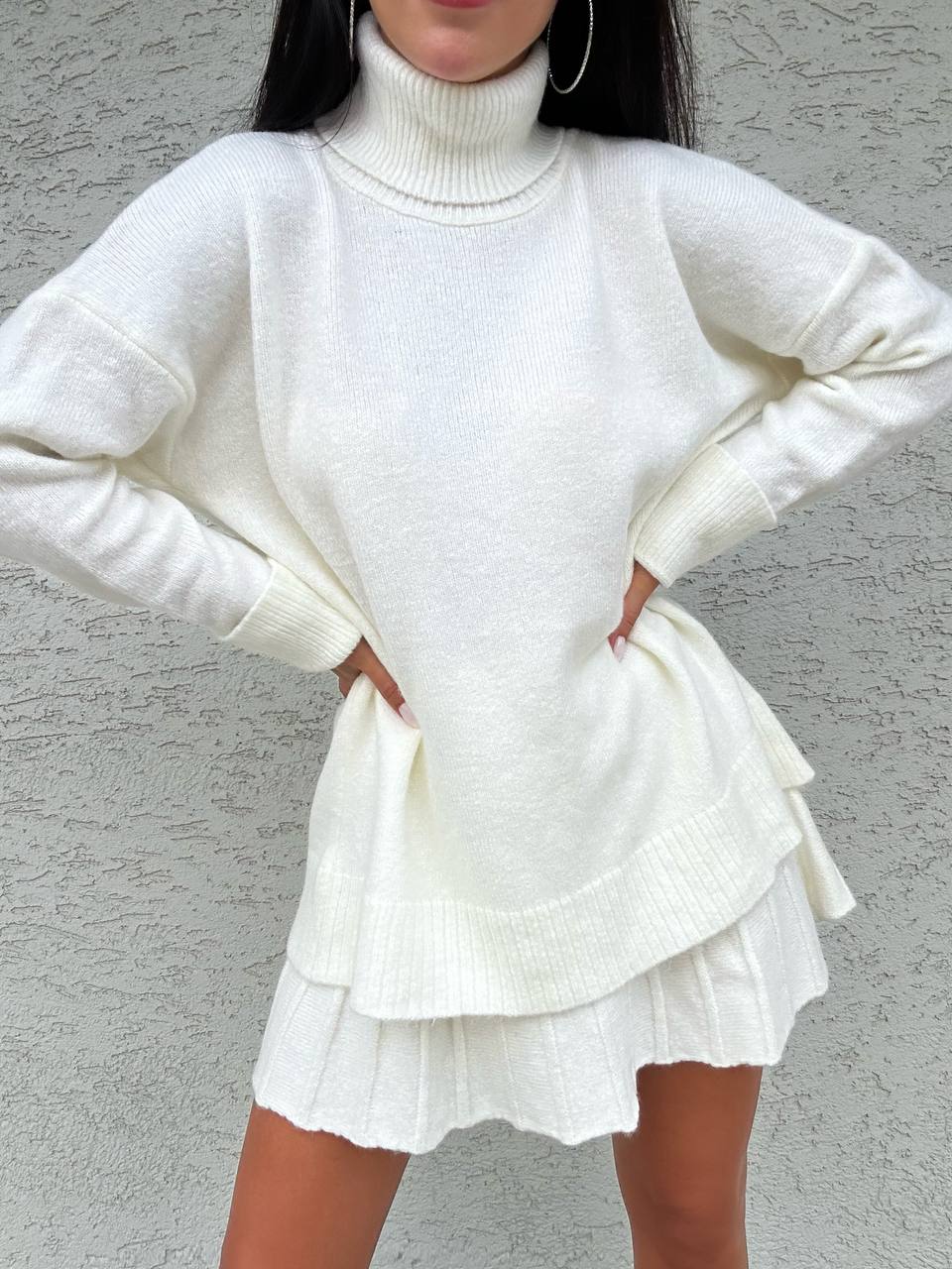 Person wearing a white sweater and skirt set against a gray background