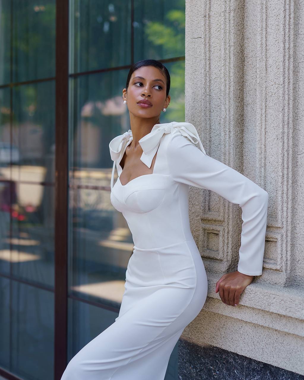 Woman in a white dress leaning against a building wall.