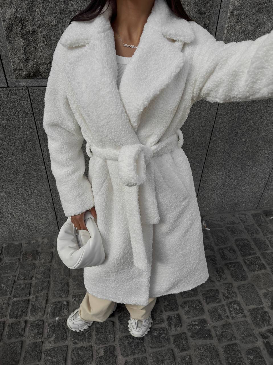 Person wearing a white plush robe on a stone pavement.