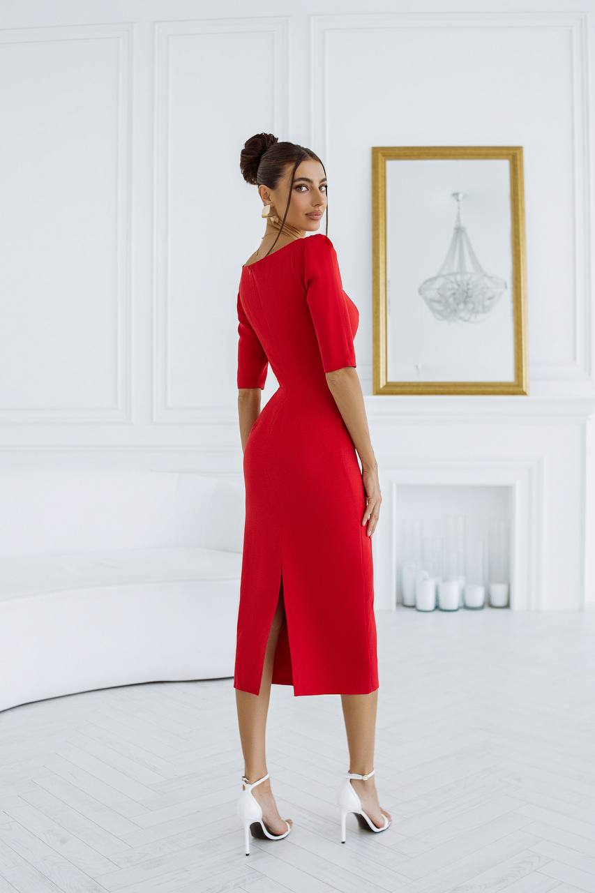 Woman in a red dress standing in a room with a white wall and framed picture.