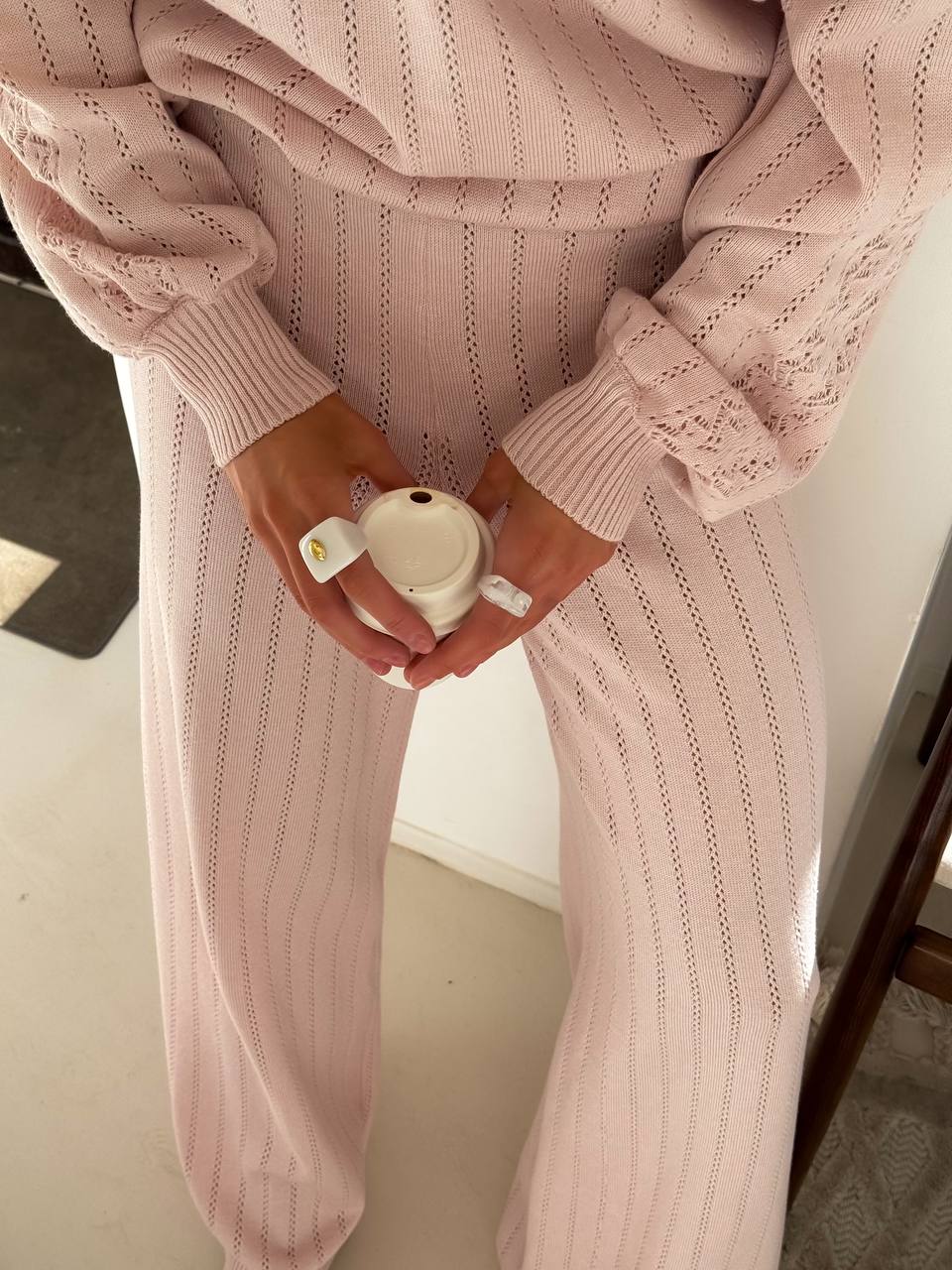 Person wearing a pink knitted outfit holding a small white cup.