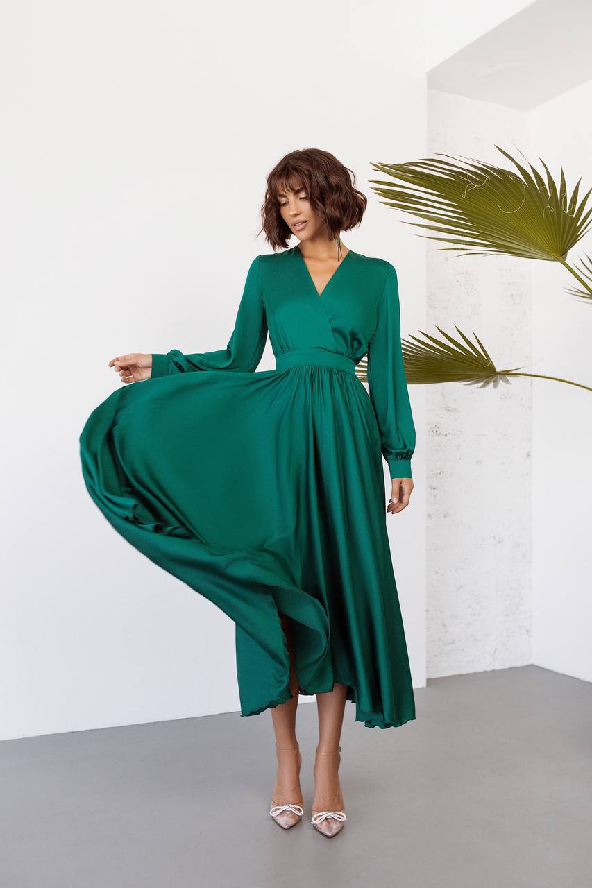 Woman wearing a green dress in a minimalistic setting with a white wall and gray floor.