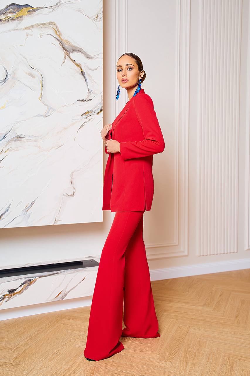 Woman in a red suit standing in a room with a marble wall and wooden floor.