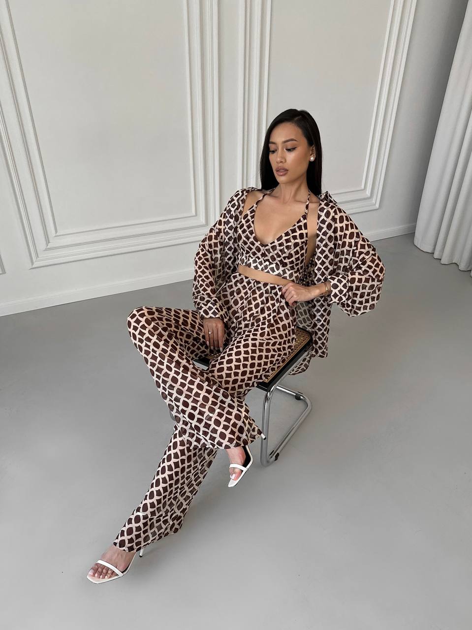 Woman in a leopard print outfit sitting on a chair in a room with white walls and gray floor.