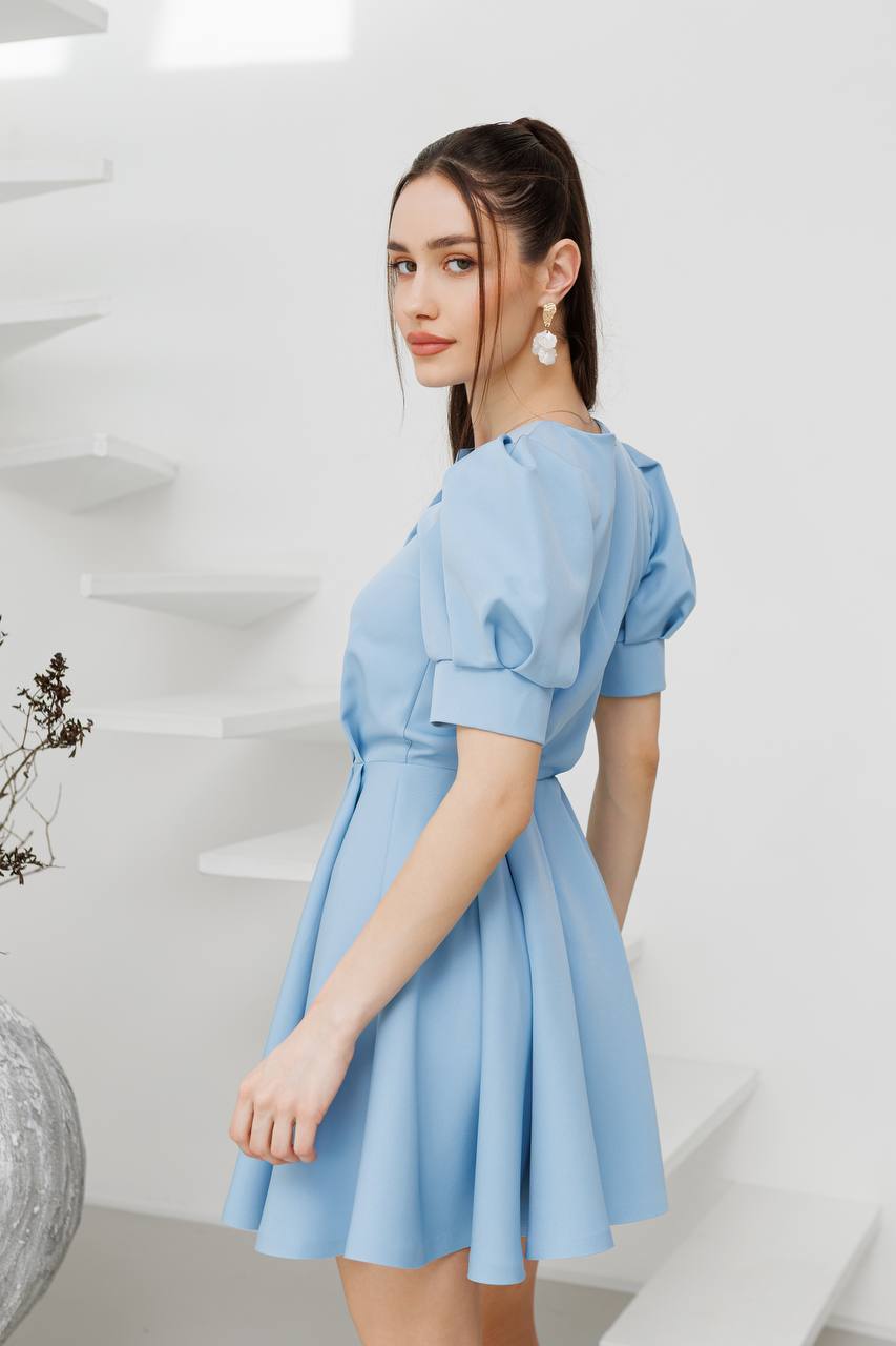 Woman wearing a light blue dress with puffed sleeves in a modern interior setting