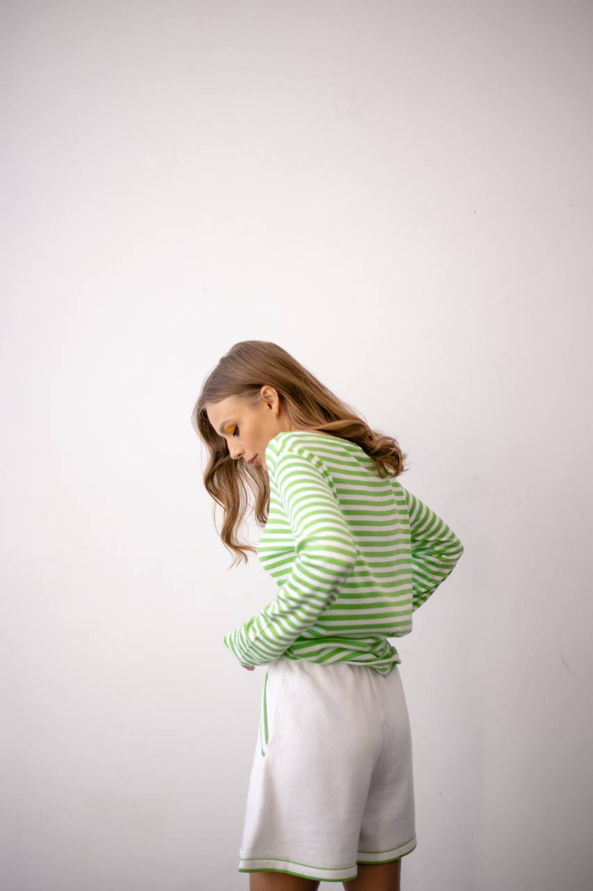 Woman wearing a green and white striped sweater and white skirt against a plain background