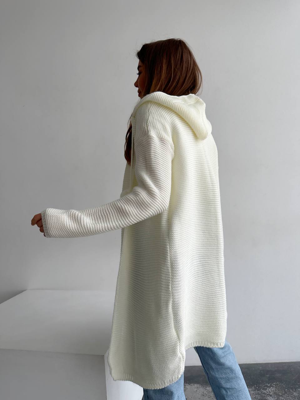 Person wearing a long cream cardigan in a minimalistic setting