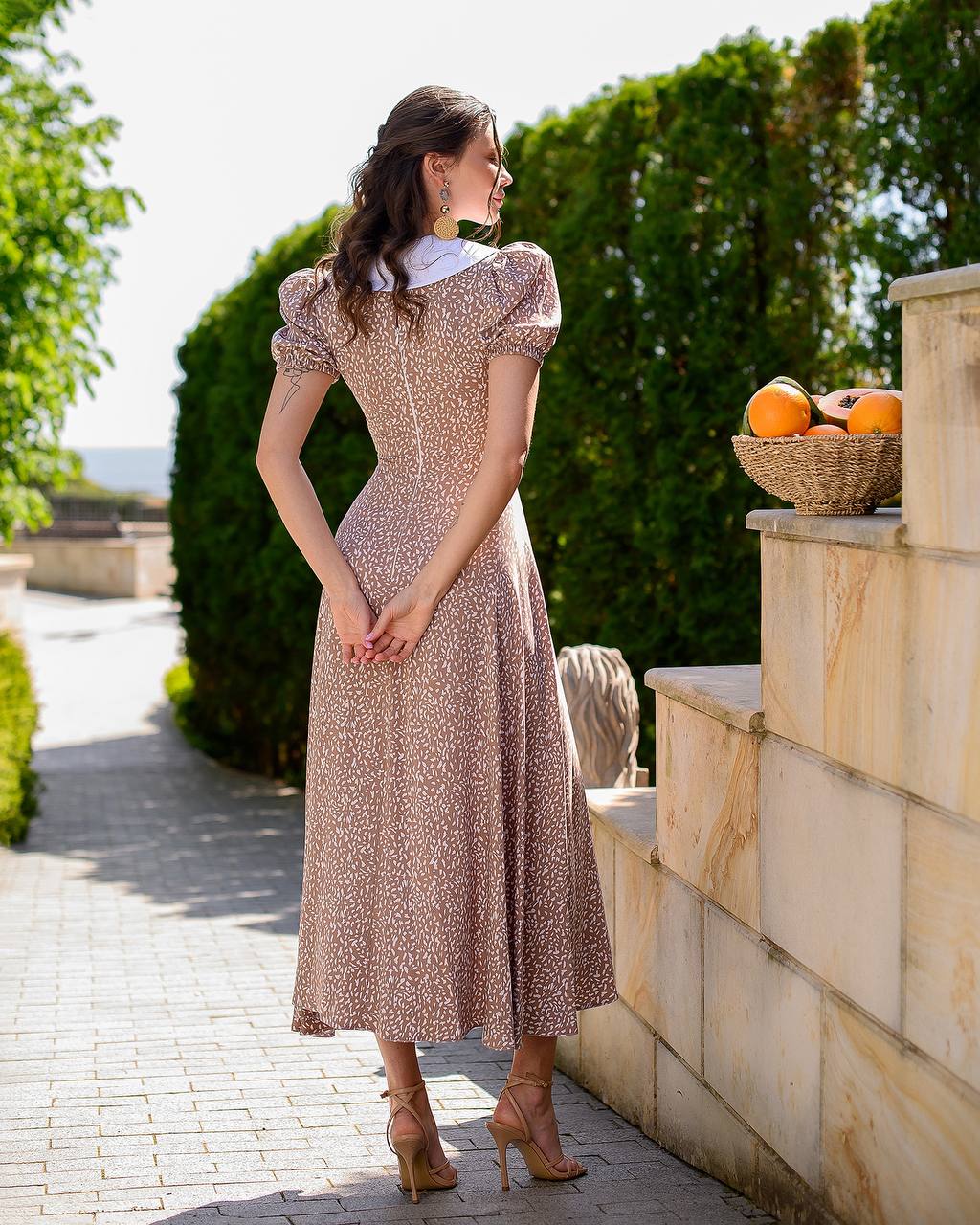 Woman in a patterned dress standing outdoors near stone steps and greenery
