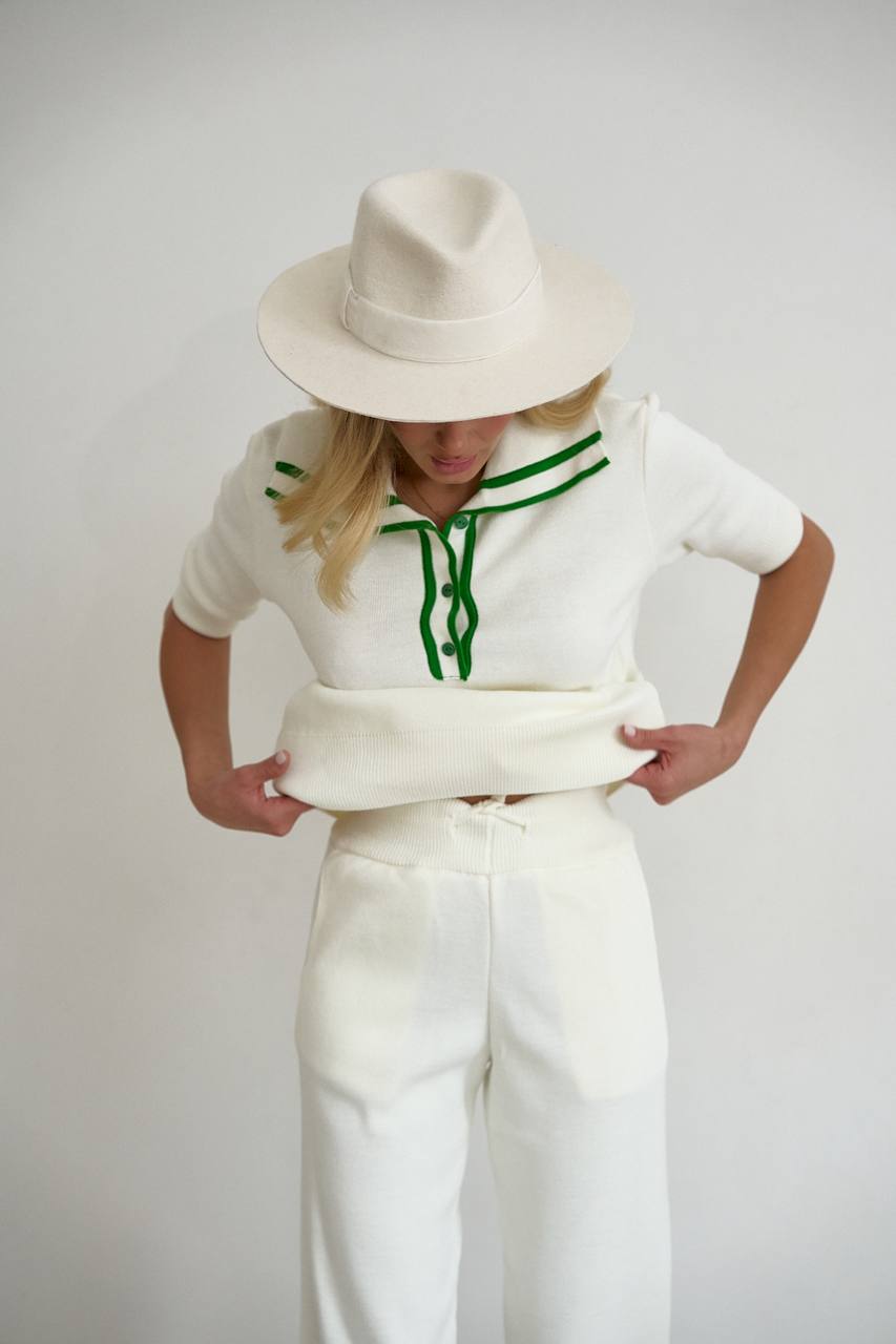 Person wearing a white sweater with green accents and white pants on a plain background