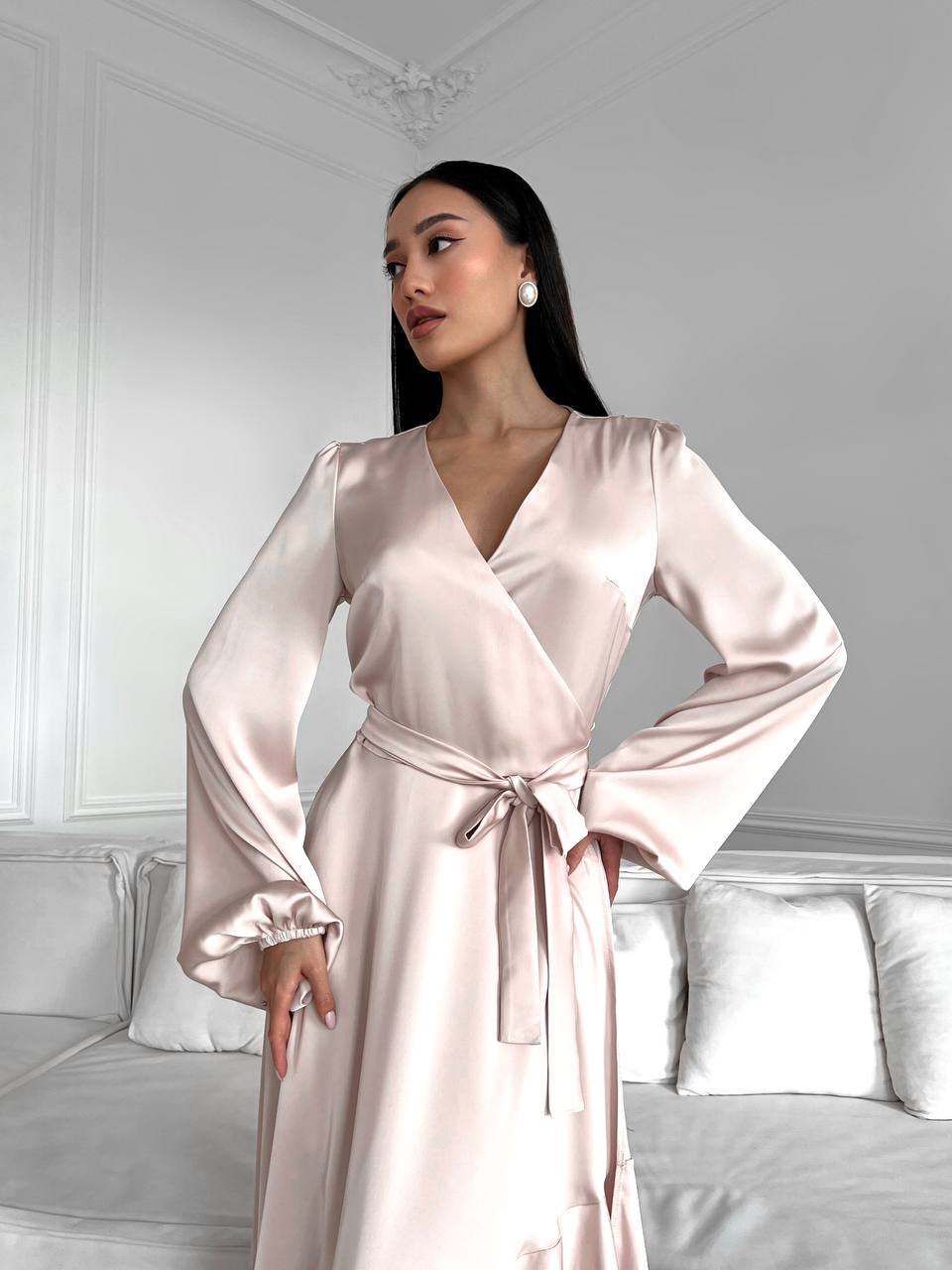 Woman wearing a light pink satin robe in a bedroom setting.