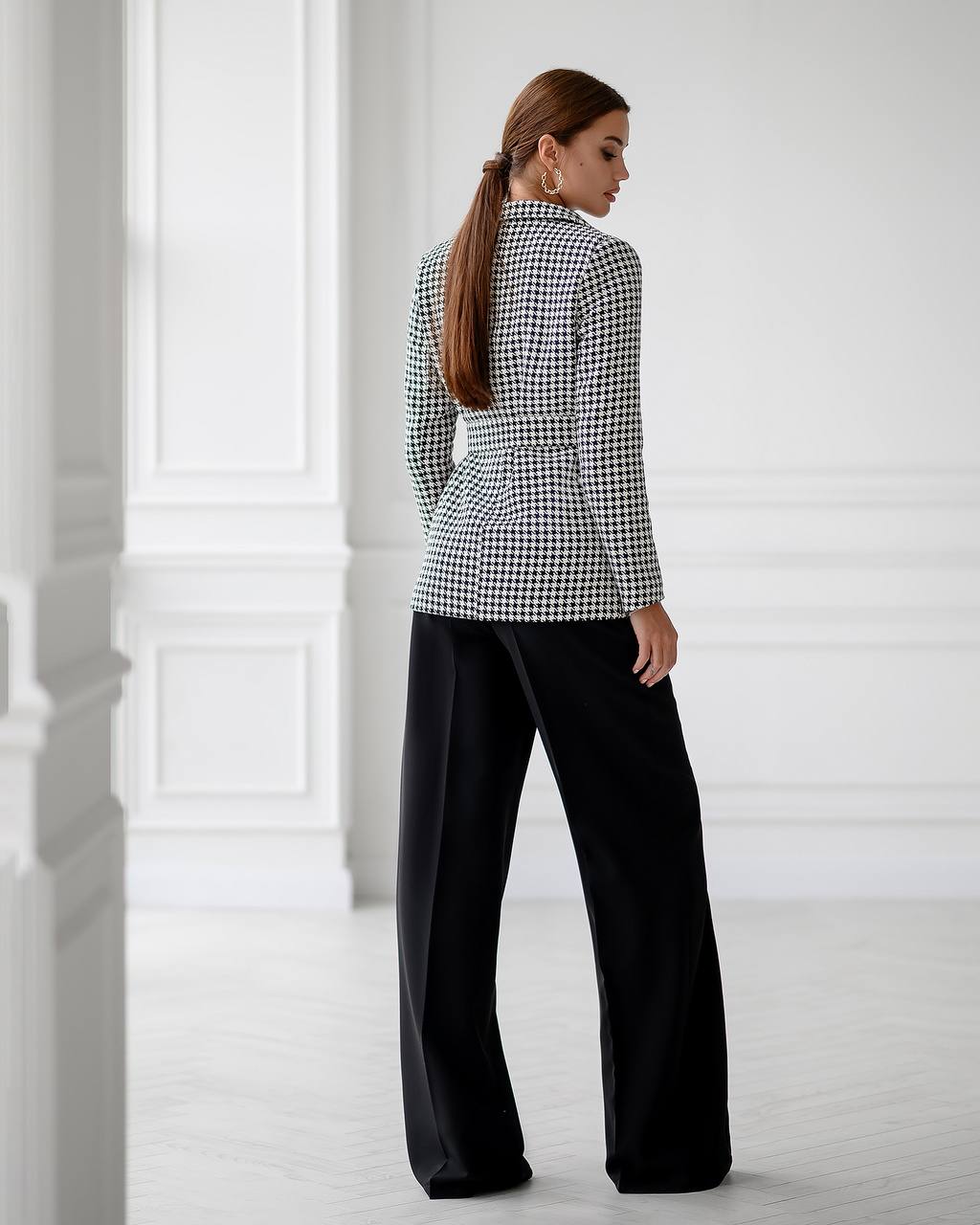 Woman wearing a black and white checkered blouse and black pants in a minimalistic setting