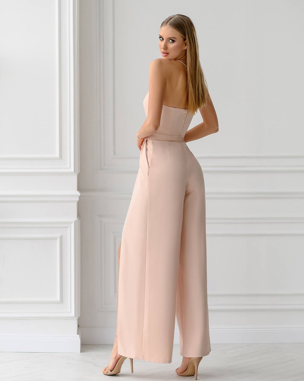 Woman wearing a pink jumpsuit standing against a white wall.