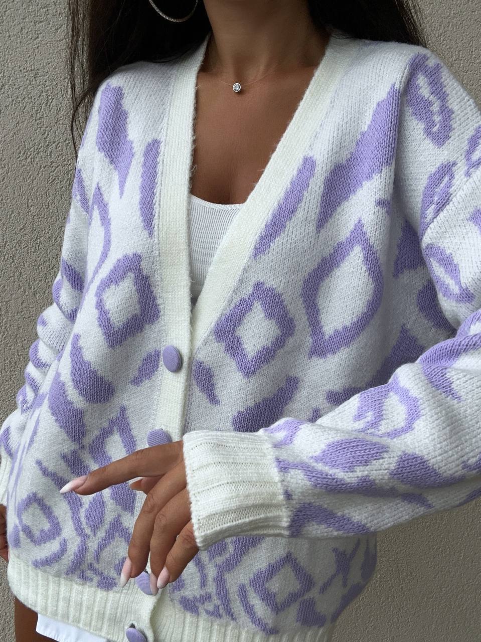 White cardigan with purple geometric pattern worn by a person against a neutral background
