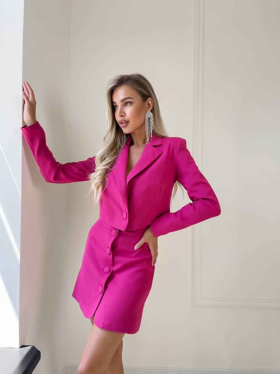 Woman wearing a bright pink suit standing against a neutral wall.