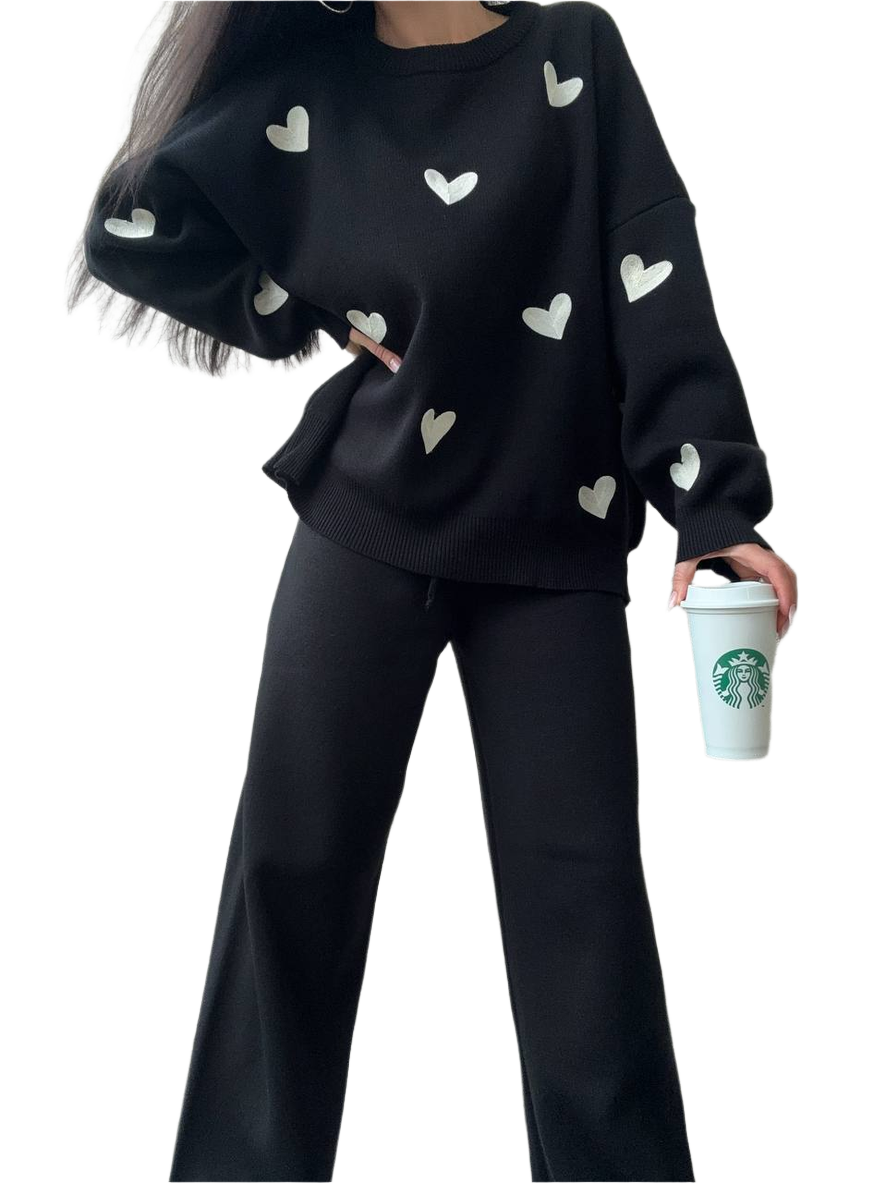 Person wearing a black sweater with heart patterns and holding a Starbucks cup on a white background
