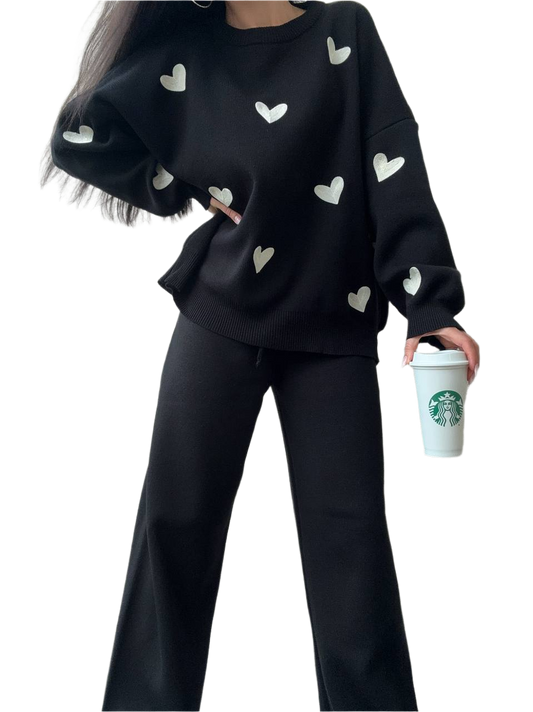 Person wearing a black sweater with heart patterns and holding a Starbucks cup on a white background