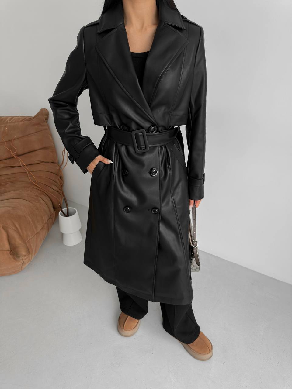 Person wearing a black leather trench coat in a minimalistic room.