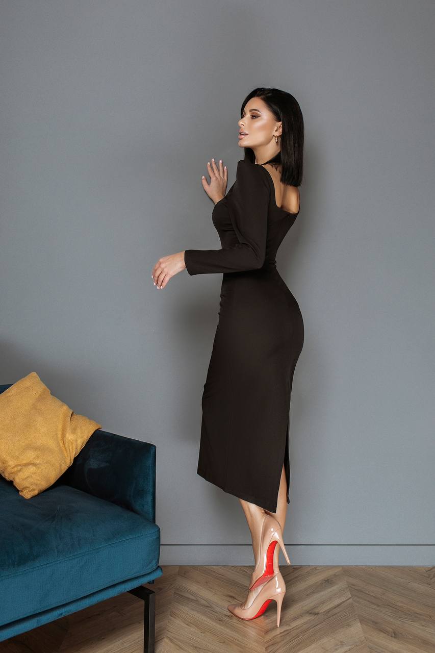 Woman in a black dress standing in a room with a blue couch and yellow pillow.