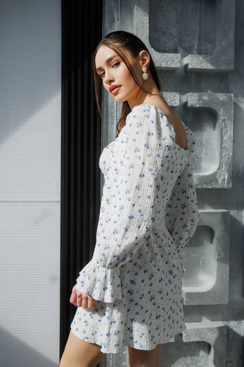 Woman in a floral dress standing against a textured wall.